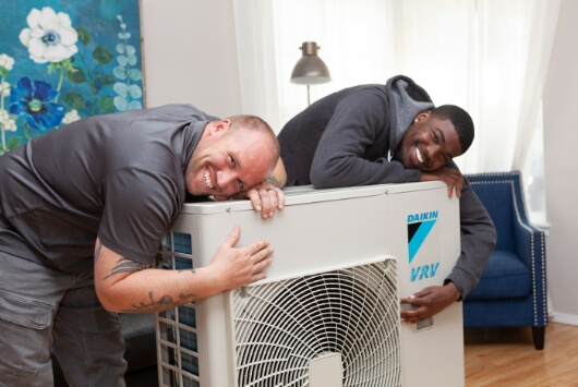 Two technicians hugging a Daikin VRV Unit.