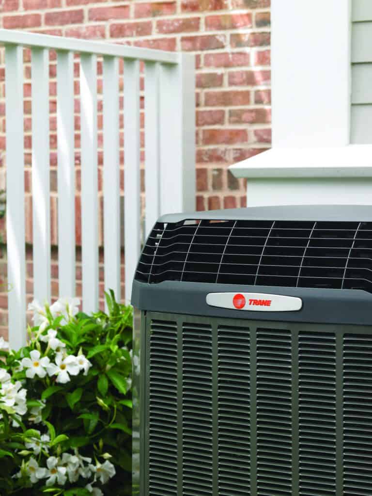 Air conditioner installation unit beside a home porch with flowers and brick exterior.