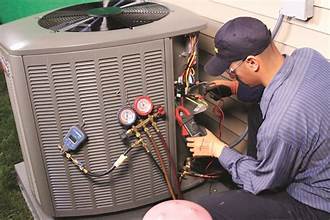 AC maintenance technician servicing an outdoor air conditioner unit with gauges and tools attached.