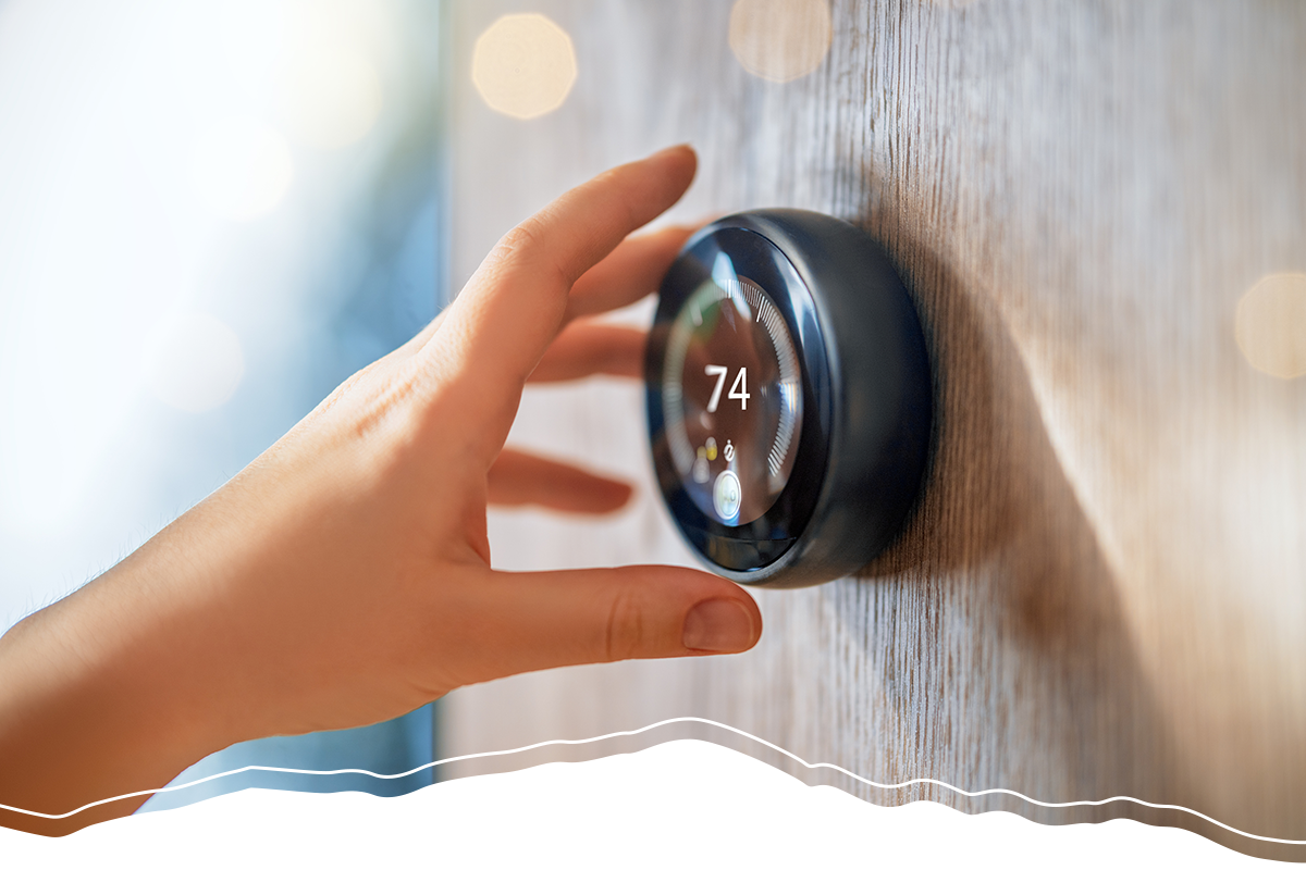 A hand reaching to a smart thermostat. There is a graphic of a mountain range at the bottom of the image, reflecting the company's branding